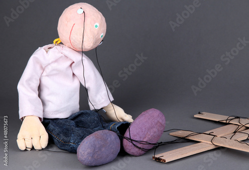 Photo: Wooden puppet sitting on grey background Wooden puppet sitting on grey background