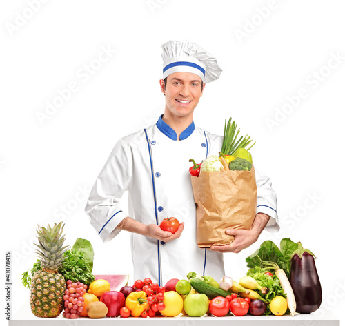 Photo: Chef holding a tomato and bag behind a table full of fruits and Chef holding a tomato and bag behind a table full of fruits and
