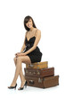 A girl in a black short dress sitting on suitcases