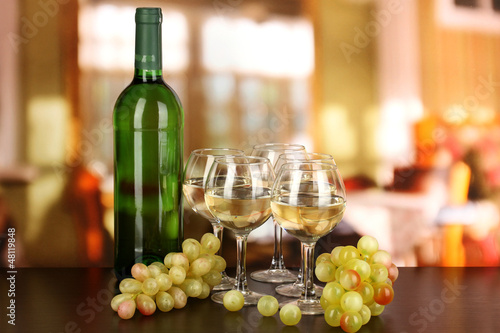 Photo: White wine in glass and bottle on room background White wine in glass and bottle on room background