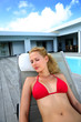 Blond woman in red bikini relaxing by pool