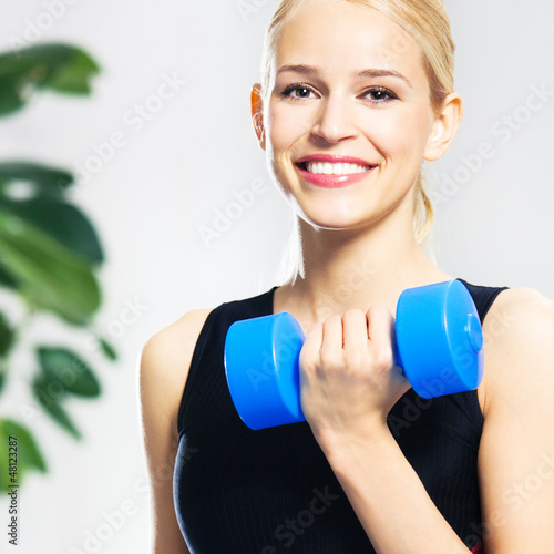Photo: Young happy smiling woman with dumbbells, indoors Young happy smiling woman with dumbbells, indoors