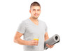 A male holding a glass of juice and a mat after an excerise