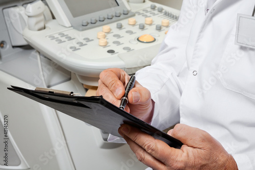 Photo: Male Doctor Writing On Clipboard Male Doctor Writing On Clipboard