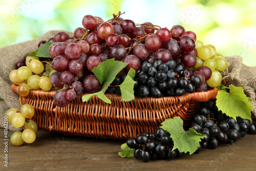 Photo: assortment of ripe sweet grapes in basket, on green background assortment of ripe sweet grapes in basket, on green background