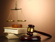 Golden scales of justice, gavel and books on brown background