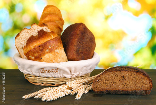 Photo: Fresh bread in basket on wooden table on natural background Fresh bread in basket on wooden table on natural background