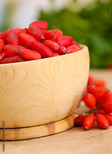 Photo: ripe barberries in wooden bowl with green leaves, on table ripe barberries in wooden bowl with green leaves, on table