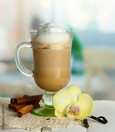 Photo: Fragrant coffee latte in glass cup with spices, on wooden table Fragrant coffee latte in glass cup with spices, on wooden table