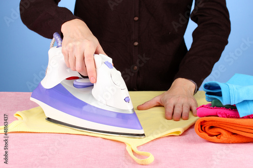Photo: Young woman ironing her clothes, on blue background Young woman ironing her clothes, on blue background
