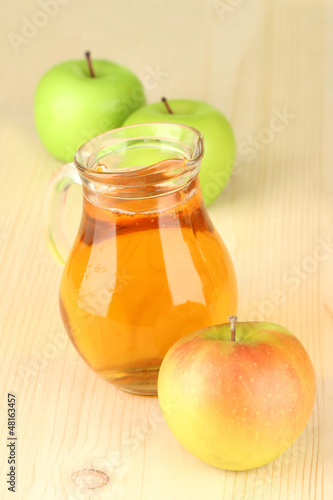 Photo: Full jug of apple juice and apple on wooden background Full jug of apple juice and apple on wooden background
