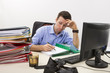 Stressed businessman filling paper documents at work