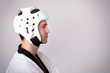 Young man with martial arts helmet standing on grey background