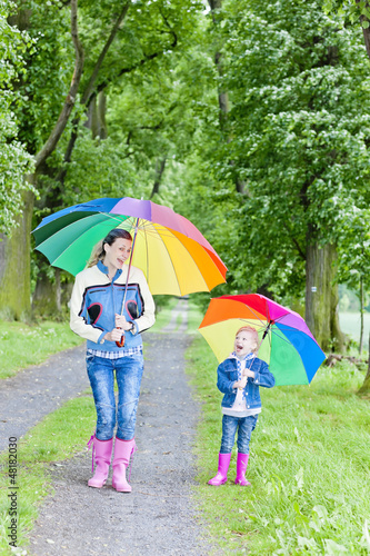Photo: mother and her daughter with umbrellas in spring alley mother and her daughter with umbrellas in spring alley