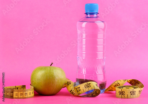 Photo: Bottle of water, apple and measuring tape on pink background Bottle of water, apple and measuring tape on pink background