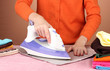 Young woman ironing her clothes, on brown background