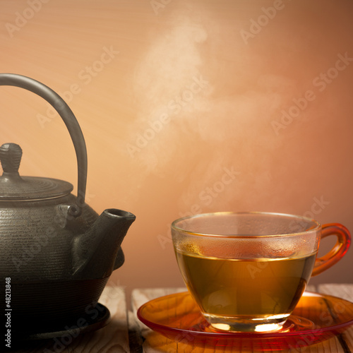 Photo: Teapot and a cup of tea on an old wooden table - hot steam smoki Teapot and a cup of tea on an old wooden table - hot steam smoki
