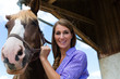 Junge Frau im Stall mit Pferd bei Sonnenschein