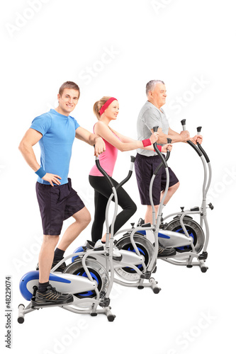 Photo: A studio shot of three people working on a cross train machine A studio shot of three people working on a cross train machine