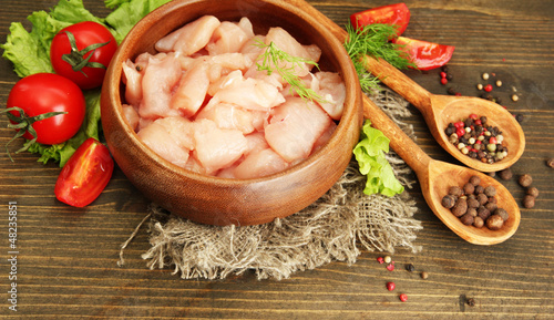 Photo: raw chicken meat in bowl, on wooden background raw chicken meat in bowl, on wooden background