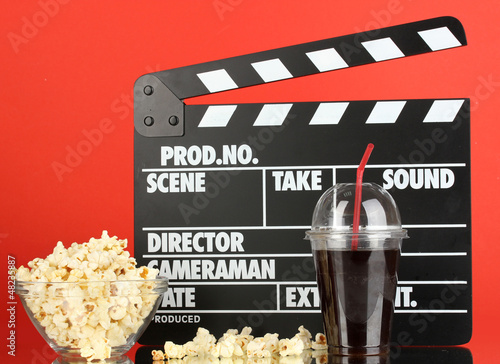 Photo: Movie clapperboard, cola and popcorn on red background Movie clapperboard, cola and popcorn on red background