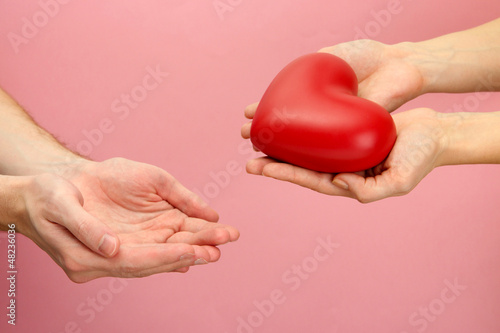 CONTENT::IMG::TITLE::Photo: Red heart in woman and man hands, on pink background Red heart in woman and man hands, on pink background