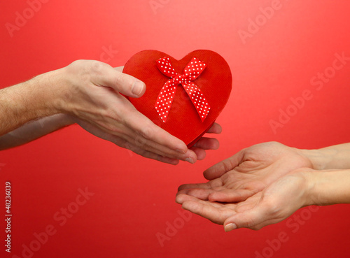 Photo: Red heart in woman and man hands, on red background Red heart in woman and man hands, on red background