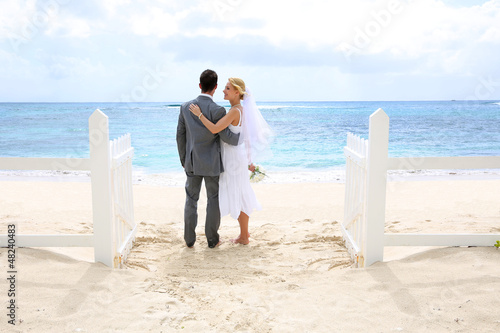Photo: Just married couple standing by a fence towards this ocean Just married couple standing by a fence towards this ocean