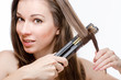 Foto: Young woman curling hair with hair straightener Young woman curling hair with hair straightener