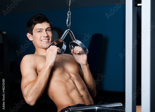 Photo: Athletic young man works out on training apparatus in gym Athletic young man works out on training apparatus in gym