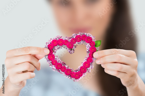 Photo: Young smiling woman holding red heart made of flowers. Focus on Young smiling woman holding red heart made of flowers. Focus on