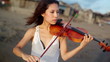 young girl playing on violin standing on the beach