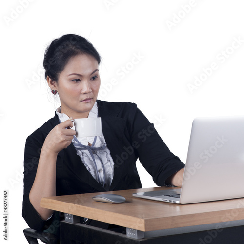 Photo: Business woman holding a cup of coffee and looking at laptop scr Business woman holding a cup of coffee and looking at laptop scr