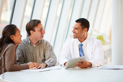 Photo: Doctor Using Tablet Computer Discussing Treatment With Patients Doctor Using Tablet Computer Discussing Treatment With Patients