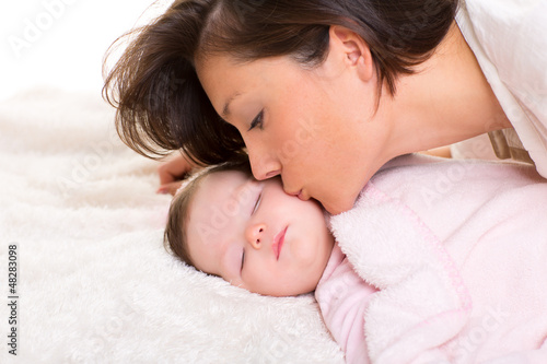 Photo: Baby girl and mother kissing her lying happy on white Baby girl and mother kissing her lying happy on white