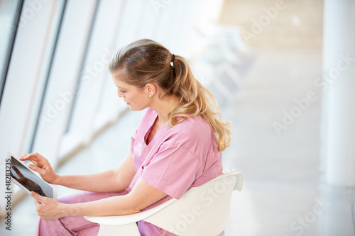 Photo: Female Nurse Sitting In Chair Using Digital Tablet Female Nurse Sitting In Chair Using Digital Tablet