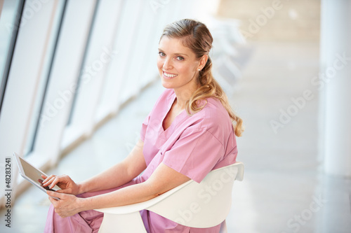 Photo: Female Nurse Sitting In Chair Using Digital Tablet Female Nurse Sitting In Chair Using Digital Tablet