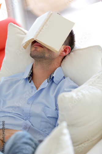 Photo: Young man sleeping in sofa with book covering his face Young man sleeping in sofa with book covering his face