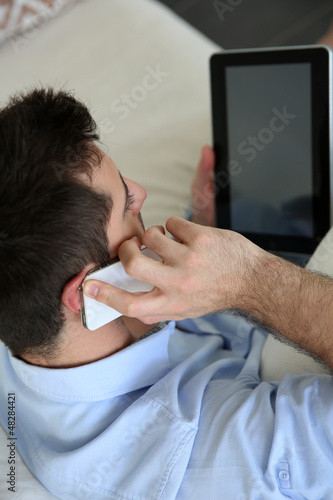 Photo: Man sitting in sofa using smartphone and tablet Man sitting in sofa using smartphone and tablet