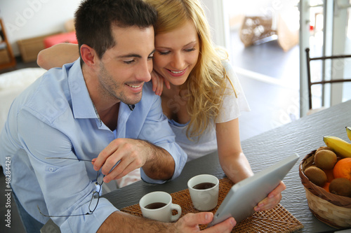 Photo: Young couple websurfing with tablet in home kitchen Young couple websurfing with tablet in home kitchen