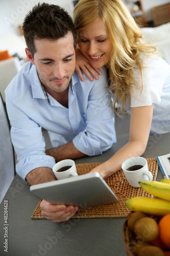 Photo: Young couple websurfing with tablet in home kitchen Young couple websurfing with tablet in home kitchen