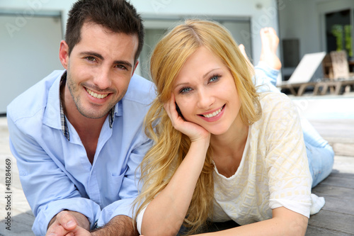Photo: Cheerful young couple sitting in front of modern house Cheerful young couple sitting in front of modern house