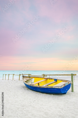 Photo: Old yellow blue wooden boat on white beach on sunset Old yellow blue wooden boat on white beach on sunset