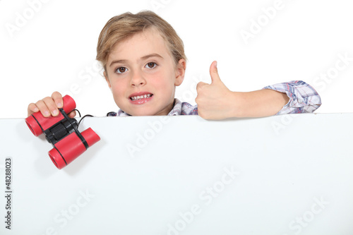 Photo: Little girl with binoculars and blank poster Little girl with binoculars and blank poster