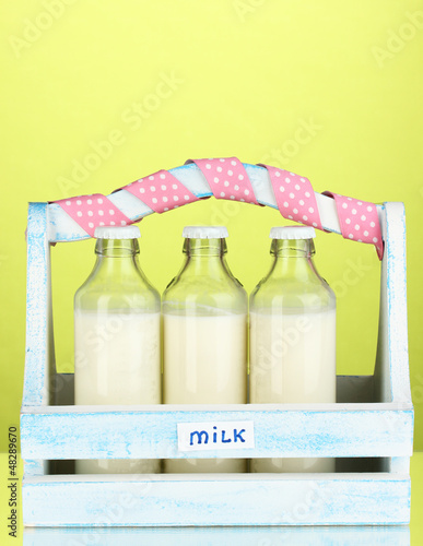 Photo: Milk in bottles in wooden box on green background Milk in bottles in wooden box on green background