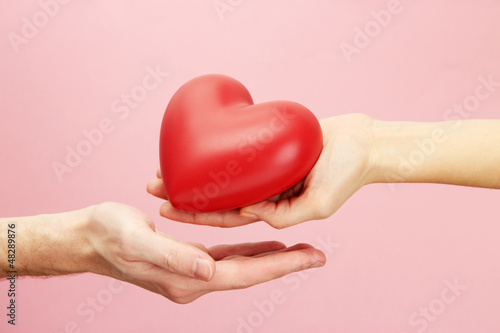 Photo: Red heart in woman and man hands, on pink background Red heart in woman and man hands, on pink background