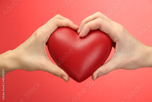 Photo: Red heart in woman and man hands, on red background Red heart in woman and man hands, on red background