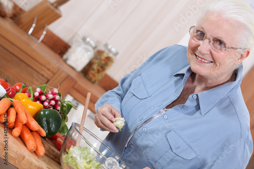 Photo: Old lady in kitchen preparing salad Old lady in kitchen preparing salad