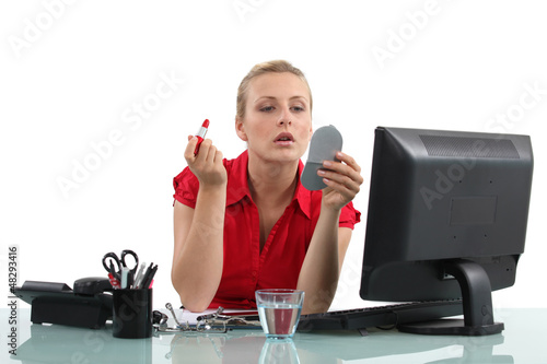 Photo: Blond woman applying lipstick in office Blond woman applying lipstick in office