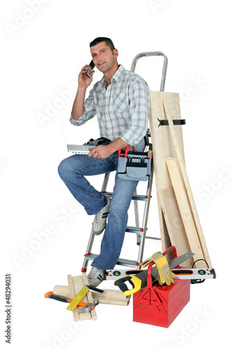 Photo: Laborer with phone and laptop sitting on a ladder Laborer with phone and laptop sitting on a ladder